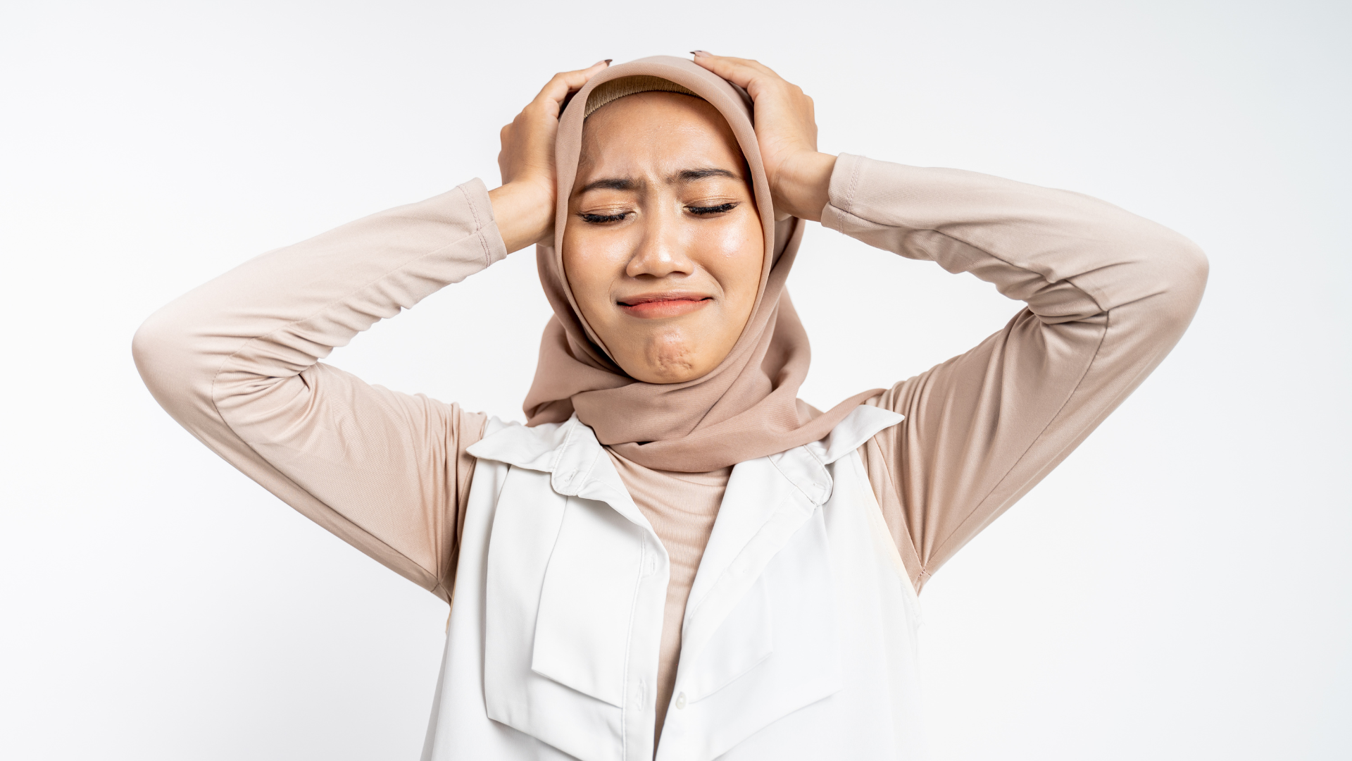 A stressed Muslim woman wearing hijab and holding her head with her hand with frustration